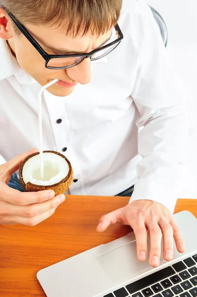 Retrato del joven sentado en su escritorio con laptop y bebiendo jugo de coco. Pedir boletos en línea para sus vacaciones. Concepto. Aislado — Foto de Stock