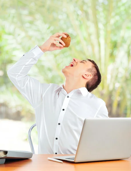 Retrato do jovem sentado em sua mesa com laptop e bebendo suco de coco. A encomendar bilhetes online para as suas férias. Conceito. Isolados — Fotografia de Stock