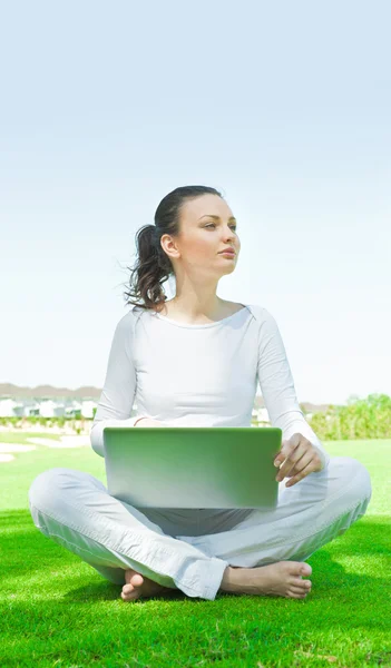 Студентка университета сидит на траве и работает на ноутбуке в кампусе — стоковое фото