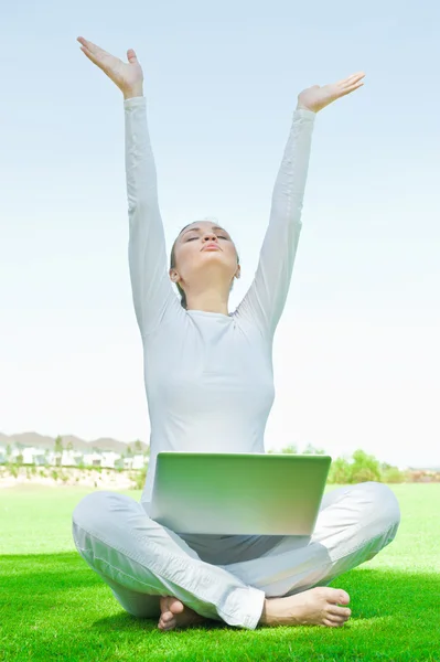 꽤 편안한 여 자가 잔디에 앉아서 그녀의 노트북에서 일 하는 동안 하늘에 그녀의 팔 목표를 스트레칭 — 스톡 사진