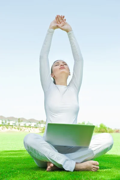 Pretty relaxed woman sitting on grass and stretching her arms aim to the sky while working on her laptop — Stock Photo, Image