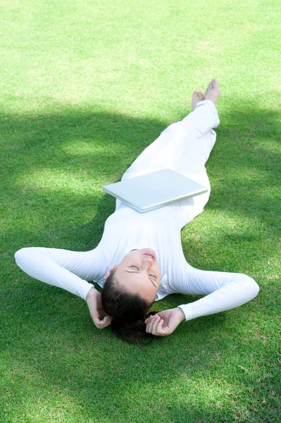Красива жінка лежить на траві з ноутбуком — стокове фото