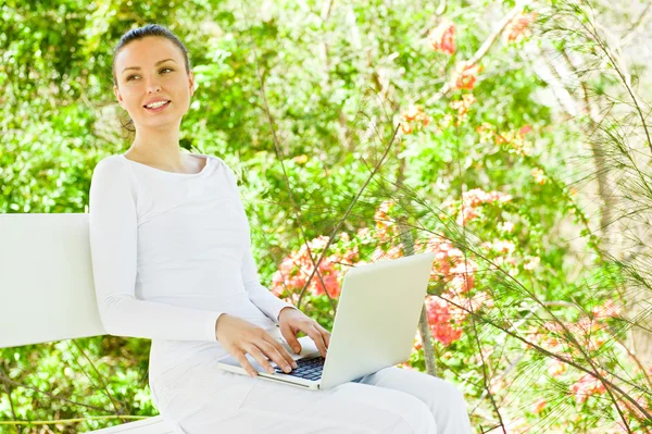 年轻漂亮的女人坐在公园长凳上的便携式计算机 — 图库照片