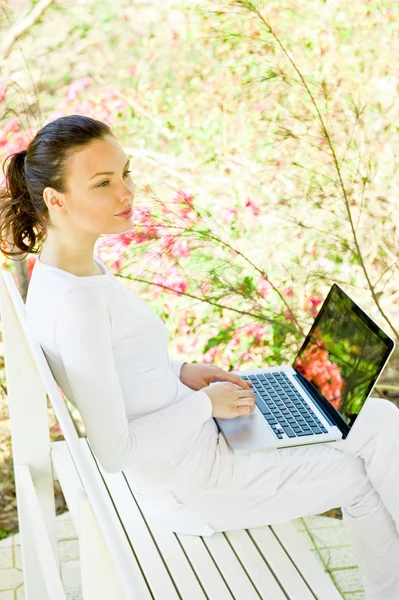 Geschäftsfrau sitzt in weißer Kleidung auf Bank und arbeitet am Laptop im Park — Stockfoto