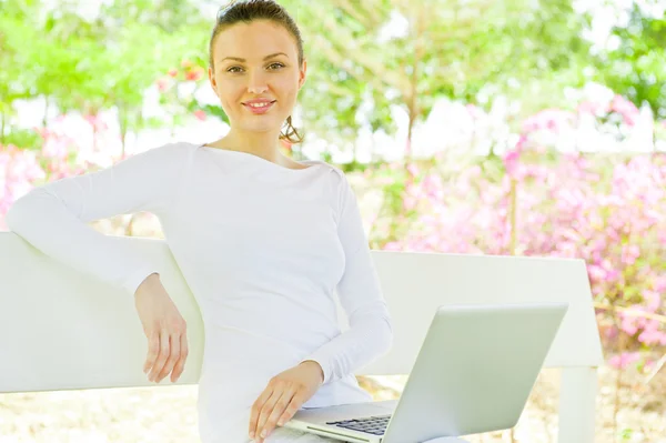 Jovem mulher bonita com laptop sentado no banco em um parque — Fotografia de Stock