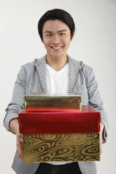 Young man carrying stack of gifts, smiling, portrait — Stock Photo, Image