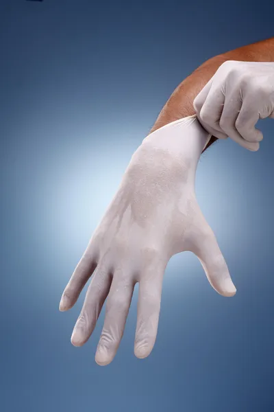 Hände ziehen OP-Handschuhe über einem kreativen blauen Hintergrund an. — Stockfoto