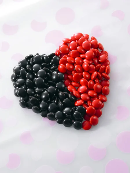 Caramelos de chocolate de color rojo y negro forman una forma de corazón — Foto de Stock