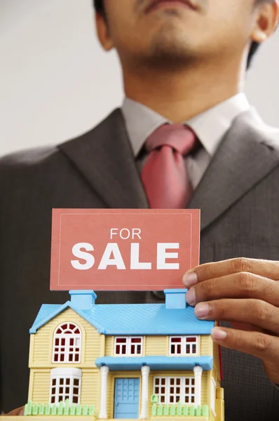 Agente imobiliário segurando um sinal de venda e uma casa modelo — Fotografia de Stock