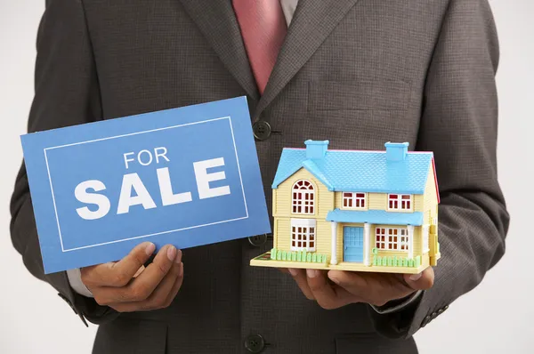 Μεσιτικό γραφείο κρατώντας ένα σημάδι για πώληση και ένα σπίτι μοντέλο — Φωτογραφία Αρχείου