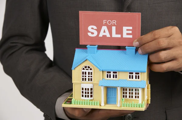 Agente de bienes raíces con un signo de venta y una casa modelo — Foto de Stock