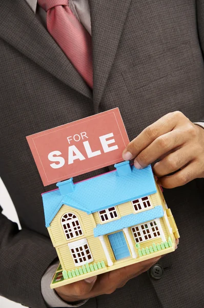 Агент з нерухомості тримає знак продажу і модель будинку — стокове фото