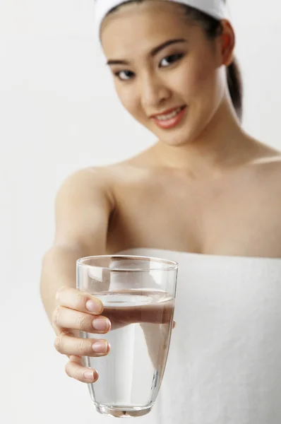 Женщина в полотенце показать стакан чистой воды — стоковое фото