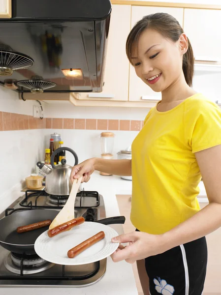 Young aldy is frying some sauseges on one hand while holding a plate — Stock Photo, Image