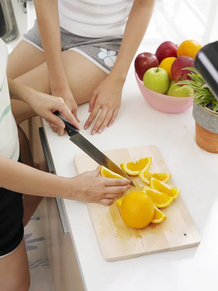 Jonge dame snijden sinaasappelen in de keuken — Stockfoto