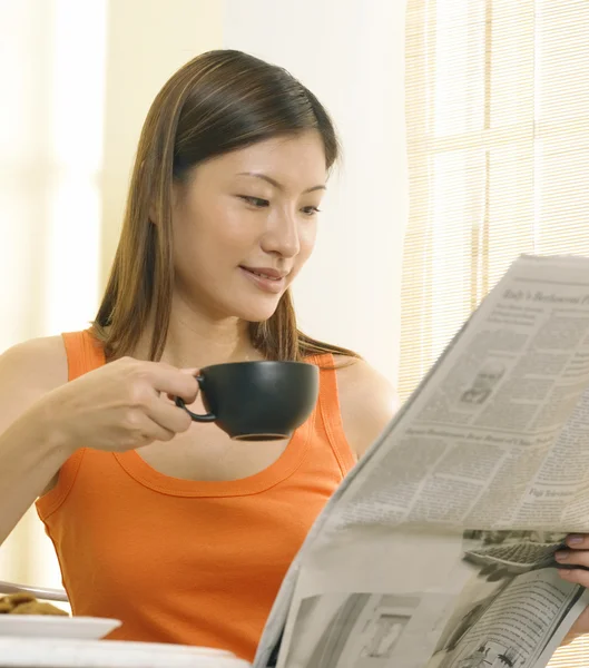 A woman is having a drink while reading the newspaper — Stock Photo, Image
