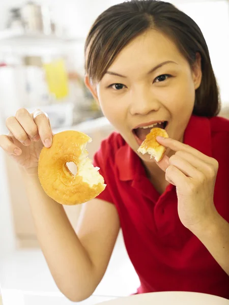 Vrouw eten donut glimlachend in de keuken — Stockfoto