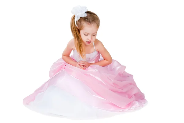 Маленька дівчинка в сукні сидить, дивлячись вниз ізольовано на білому — стокове фото
