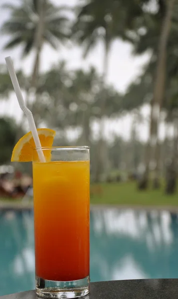 Ett glas tequila sunrise av en pool — Stockfoto