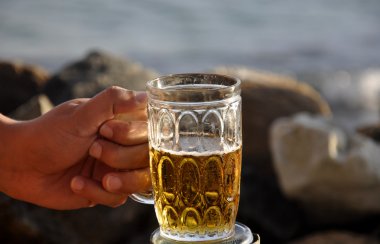 bir kupa bira bir kayalık plaj tutan bir adam