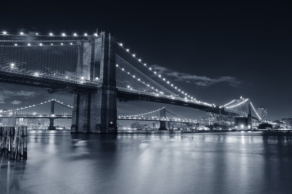 Brooklyn Bridge over East River at night in black and white in New York City Manhattan with lights and reflections.
