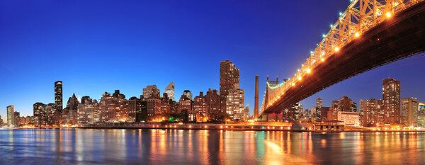 Queensboro Bridge over New York City East River at sunset with river reflections and midtown Manhattan skyline illuminated.