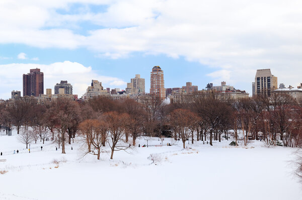 New York City Manhattan Central Park in winter with snow and city skyline with skyscrapers, blue cloudy sky.