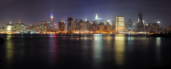 New York City Manhattan midtown panorama at night with skyscrapers illuminated over east river