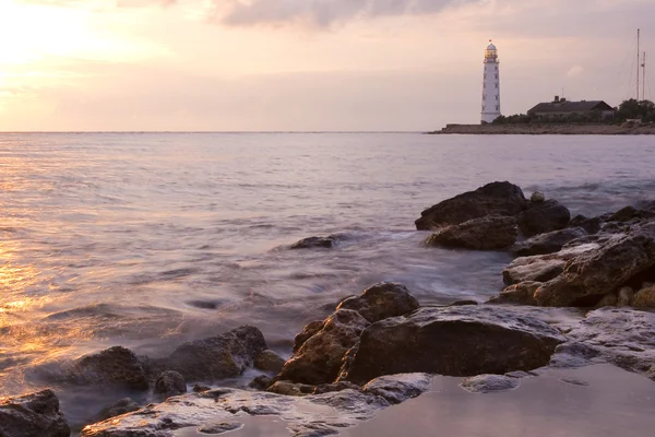 Красивий скелястий морський пляж на заході сонця з маяком — стокове фото