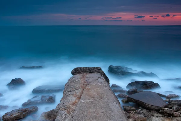 Hermosa playa de mar rocoso al atardecer con muelle roto —  Fotos de Stock