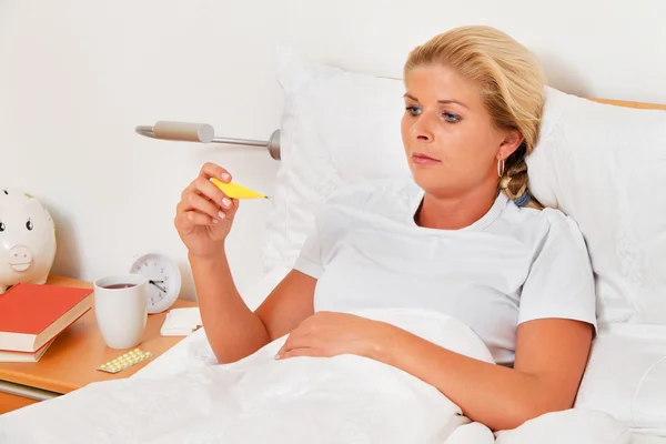 Vrouw is ziek in bed en heeft een koorts thermometer. — Stockfoto