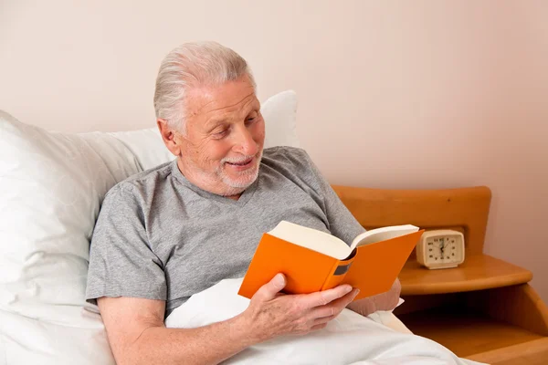 Senior v pečovatelském domě číst knihu v posteli — Stock fotografie
