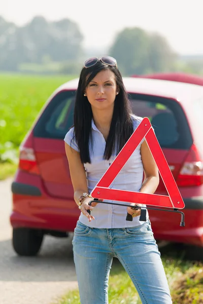 Mulher com um triângulo de aviso em caso de avaria — Fotografia de Stock