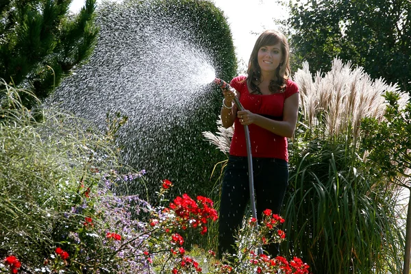 Женщина, заливающая цветы в саду — стоковое фото