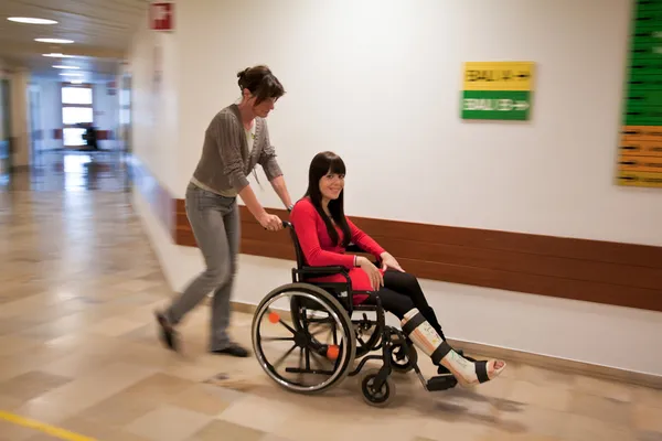 Kvinna med benet i gips och sjuksköterska rollstruhl — Stockfoto