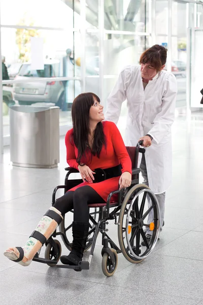 Woman with leg in plaster, wheelchair and carer — Stock Photo, Image