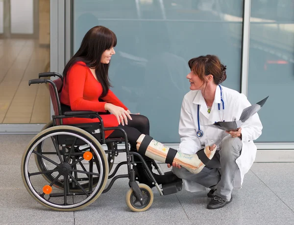 Donna con gamba in gesso, medico e sedia — Foto Stock