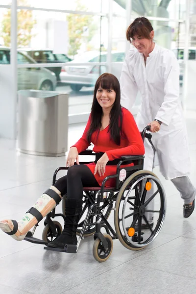 Woman with leg in plaster, wheelchair and carer — Stock Photo, Image