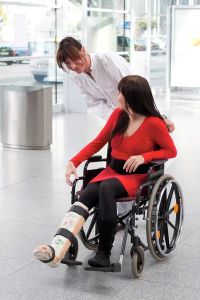 Femme avec jambe en plâtre, fauteuil roulant et soignant — Photo