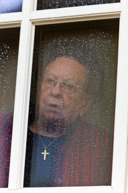 Pensive looks sad elderly woman out of a window clipart