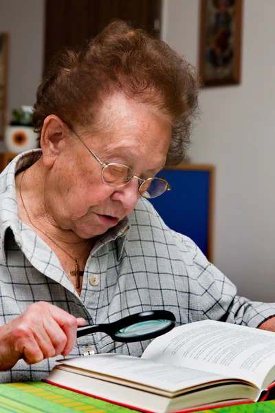 Mulher idosa lê um livro com óculos — Fotografia de Stock
