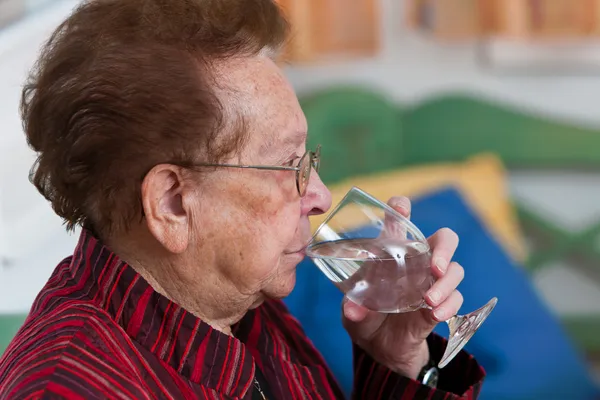 Mulher idosa bebendo água de um copo — Fotografia de Stock