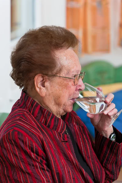 Ηλικιωμένη γυναίκα πόσιμο νερό από ένα ποτήρι — Φωτογραφία Αρχείου