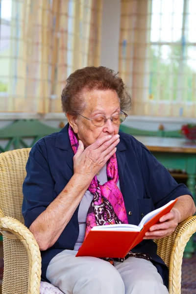 Senior está sentado em uma poltrona e lendo um livro — Fotografia de Stock