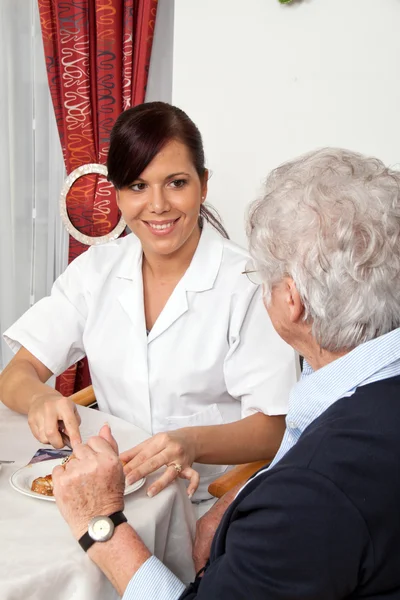 Pielęgniarka pomaga starsza kobieta na śniadanie — Zdjęcie stockowe