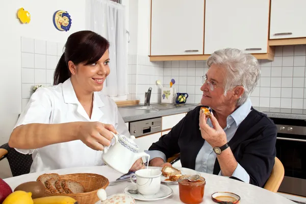 Медсестра помогает пожилой женщине за завтраком — стоковое фото