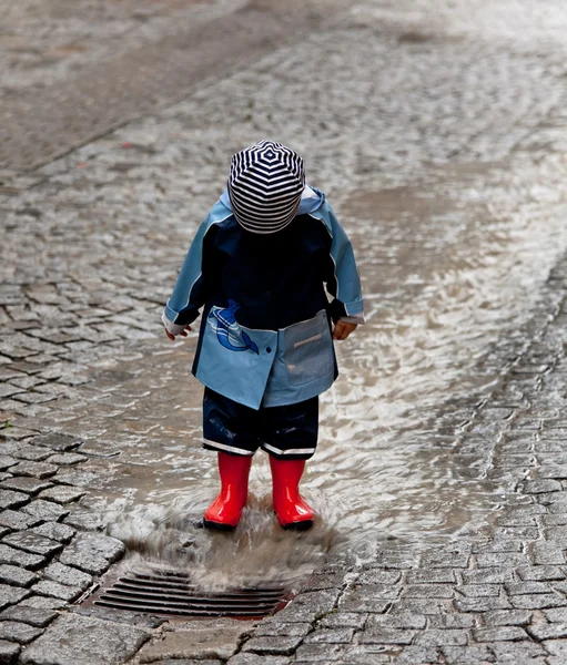 Criança se diverte com roupas de chuva na chuva — Fotografia de Stock