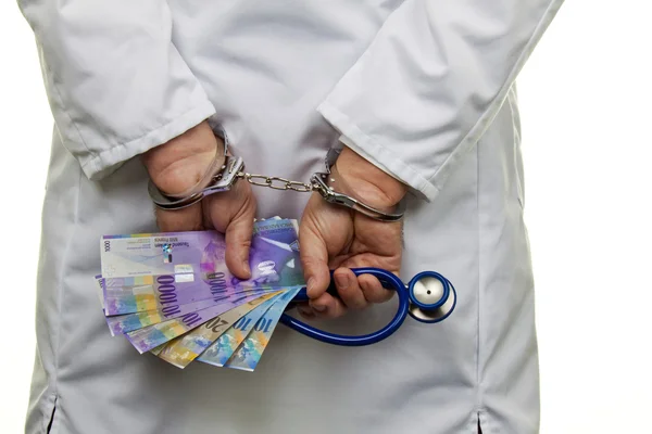 Доктор со швейцарскими банкнотами и наручниками — стоковое фото