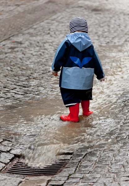 Дитина розважається з дощовим одягом під дощем — стокове фото