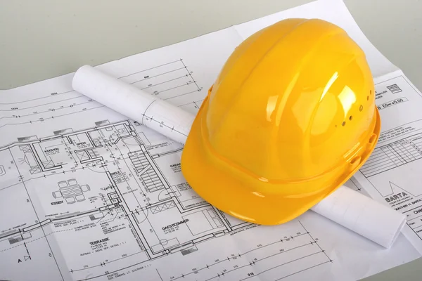 Angle shot of some construction plans and a yellow helmet — Stock Photo, Image